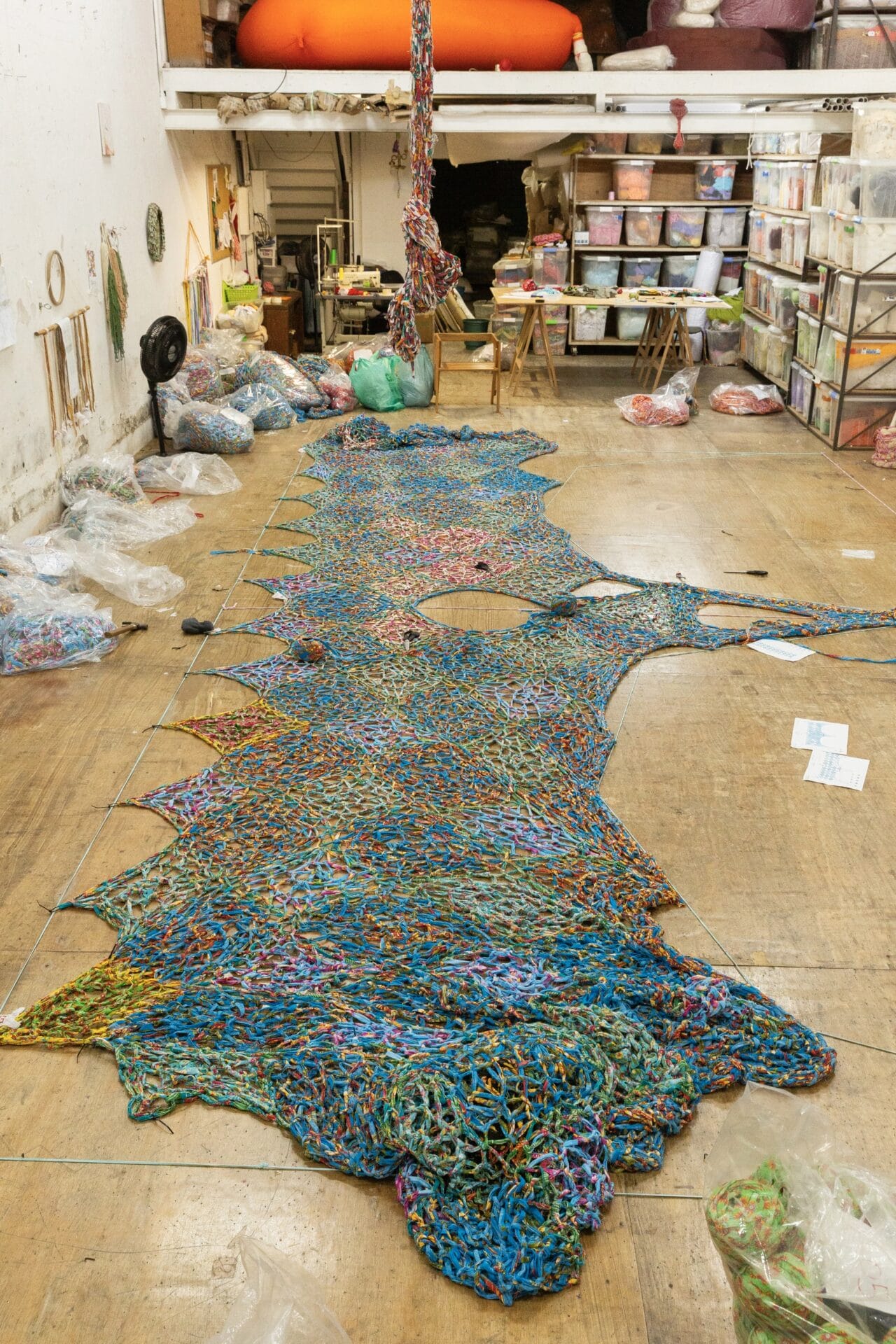 a large crocheted installation spread out on the floor of the artist's studio