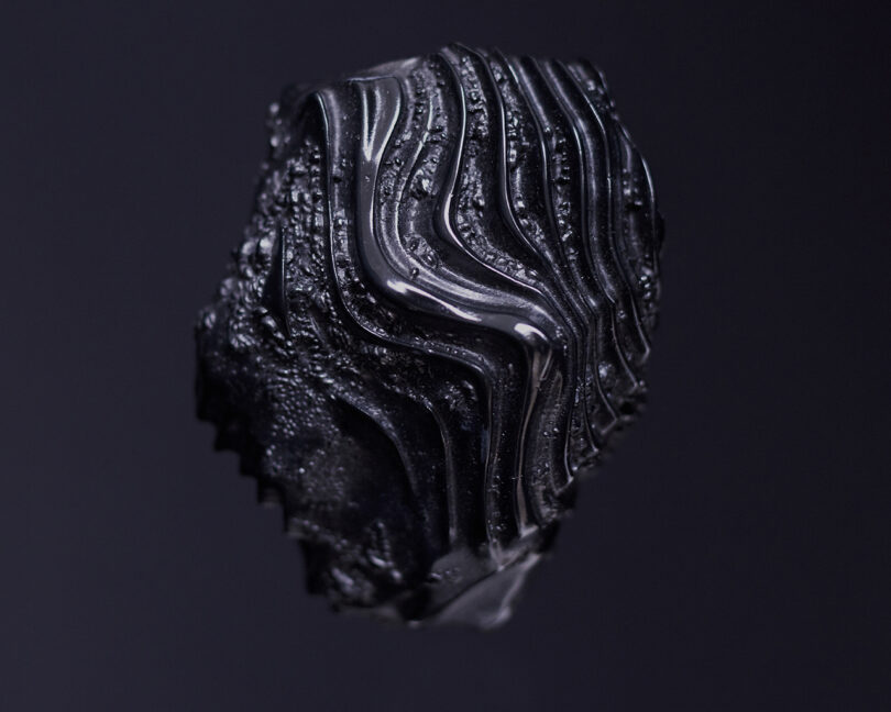 Close-up of a black object with intricate, wavy patterns on a dark background.