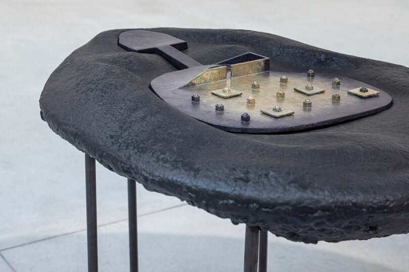 Modern abstract sculpture with an irregular black surface and industrial elements, including bolts and metallic structures.