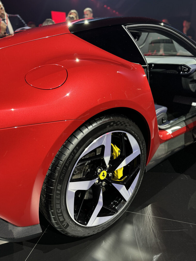 Close-up view of a red sports car's rear quarter panel and wheel, featuring a yellow Ferrari logo on the brake caliper.