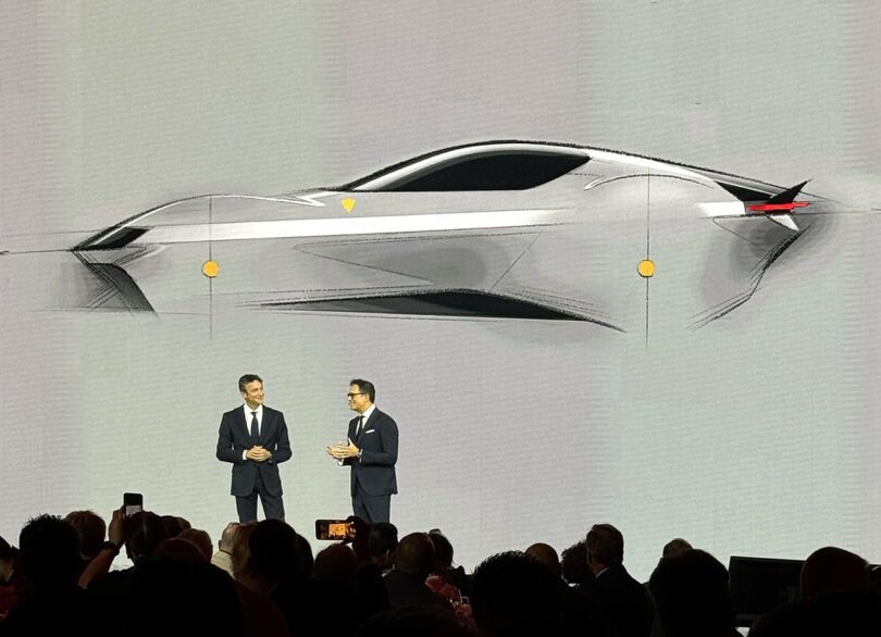 Two men in suits presenting a Ferrari 12Cilindri sports car design on a large screen at an automotive event.