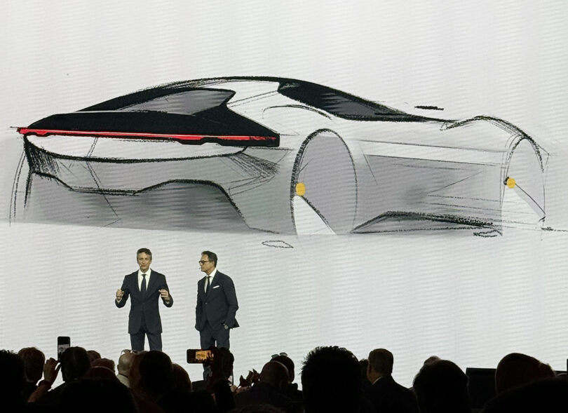 Two men presenting a Ferrari 12Cilindri sports car sketch on a large screen at an automotive event.