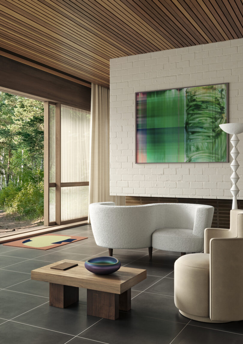 Modern living room with white sofa, beige armchair, and a wood coffee table, featuring large windows overlooking a forest, and an abstract painting on a white brick wall