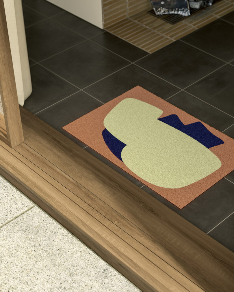 A colorful doormat with abstract design on a tiled floor by a wooden door threshold