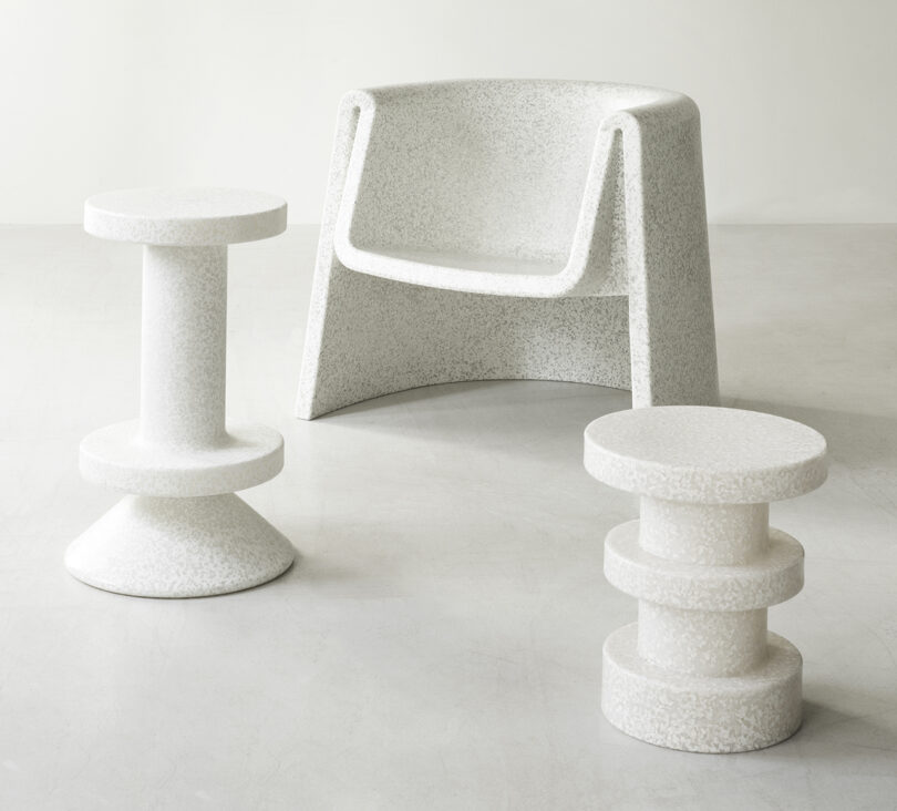 A white, speckled armchair is flanked by two matching, uniquely shaped side tables on a plain, light-colored floor.