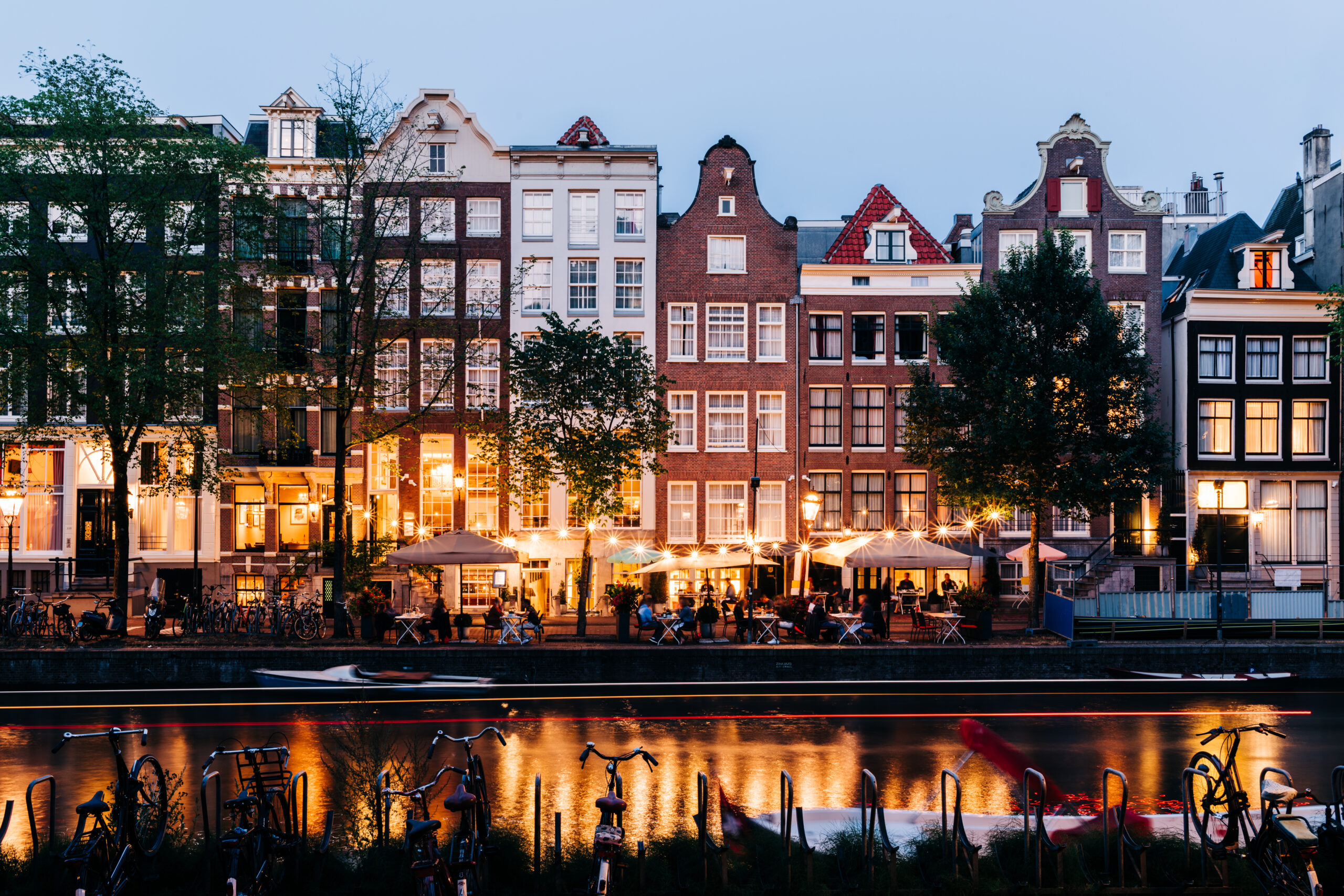 GettyImages-1337033260.jpg People sit at canalside tables outside bars and restaurants lit by string lights in the evening