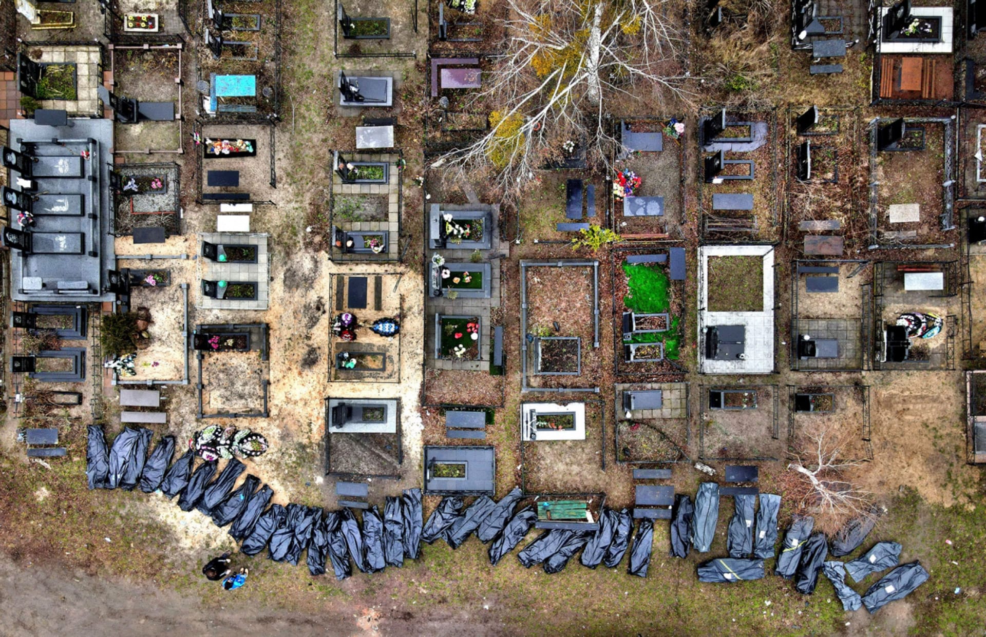 two people stand near a line of black body bags at a cemetary