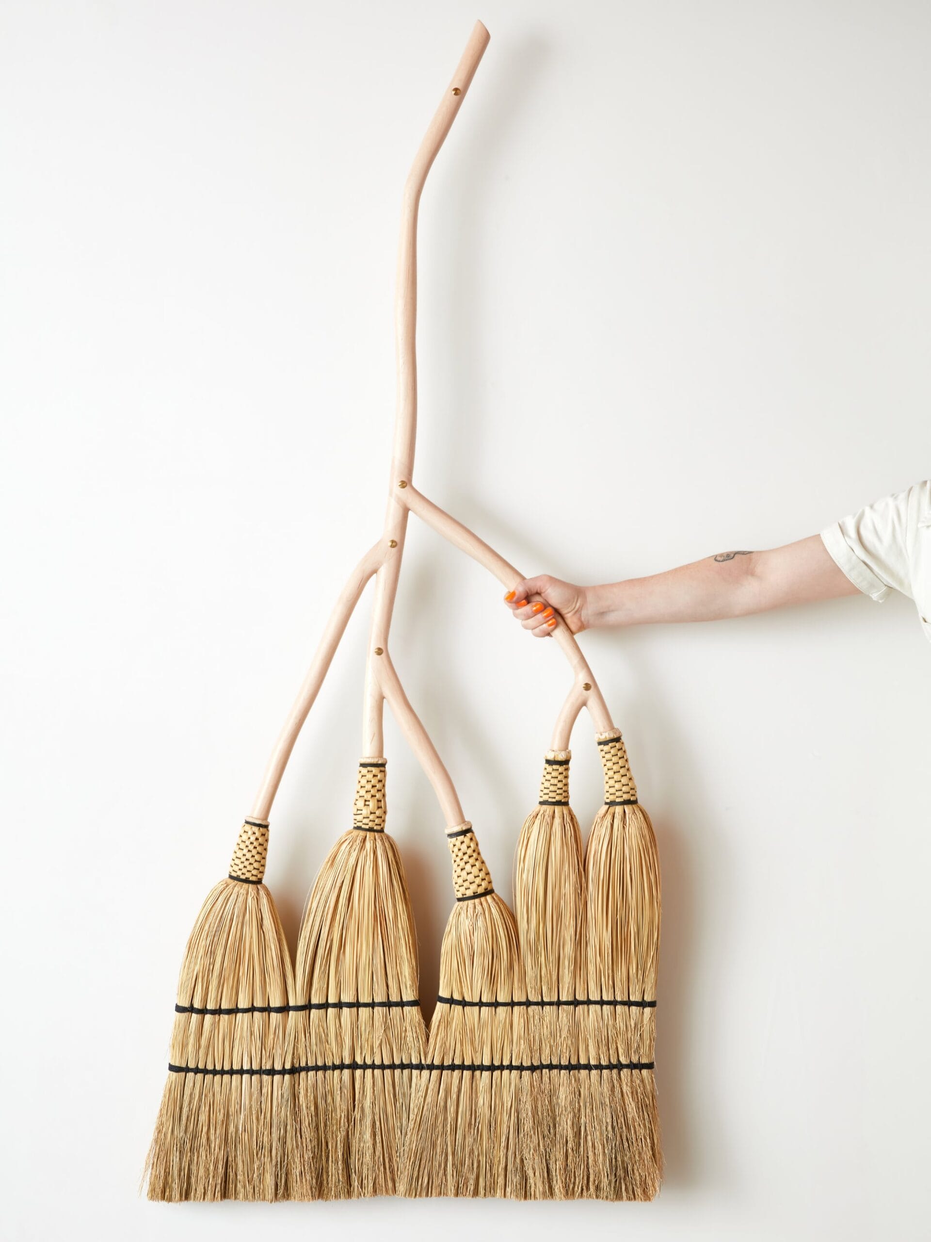 a hand reaching out to hold a broom with five brushes all connected