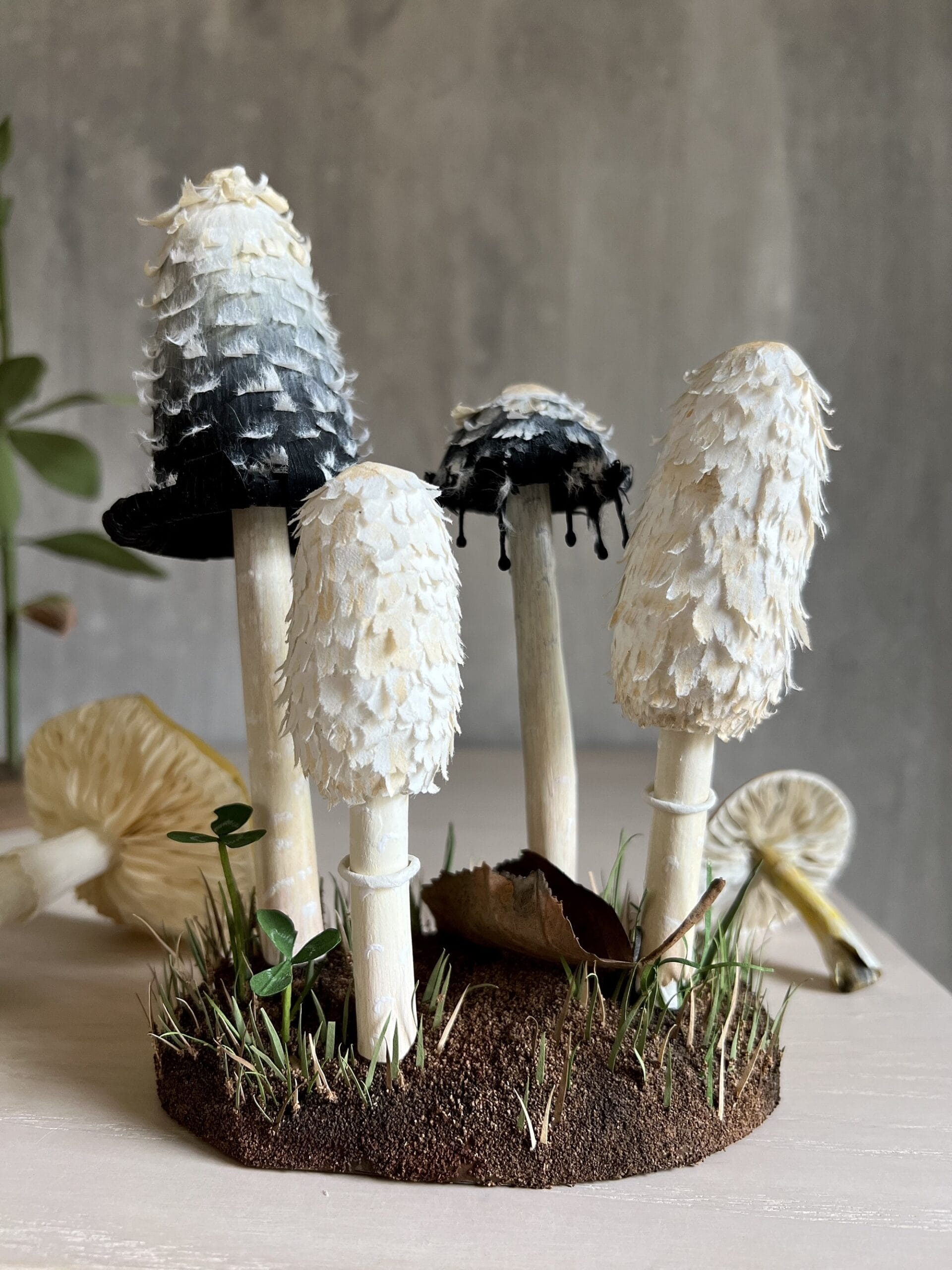 a sculpture made of paper depicting a group of mushrooms growing from a base of soil 