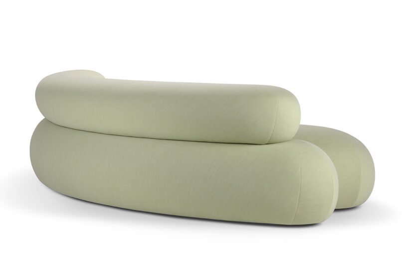 A light green modern sofa with smooth, rounded curves and a minimalist design, photographed from the back.