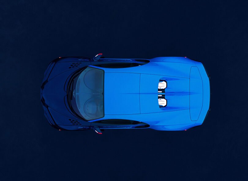 Aerial view of a blue Bugatti Chiron sports car with a sleek design, showing two visible seats and aerodynamic contours against a dark background.