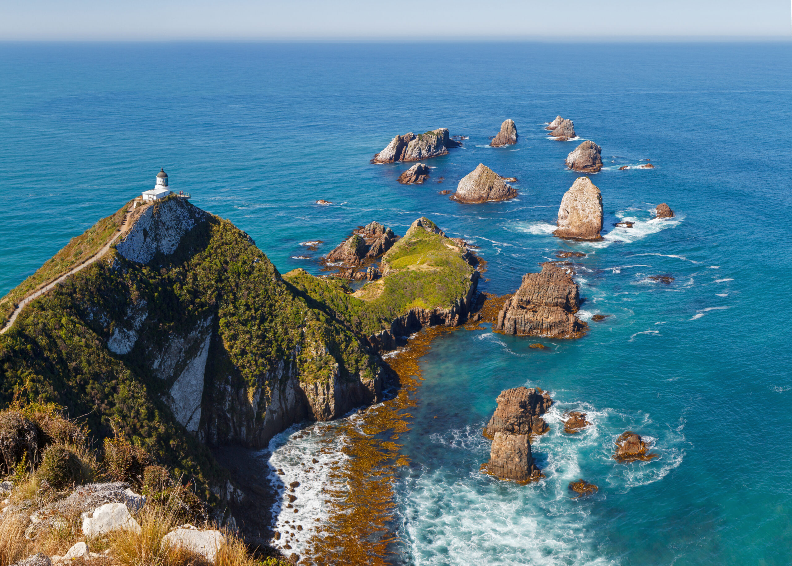 iStock-1168758516-RFE.jpg A rocky bluff in New Zealand with a lighthouse overlooking the ocean