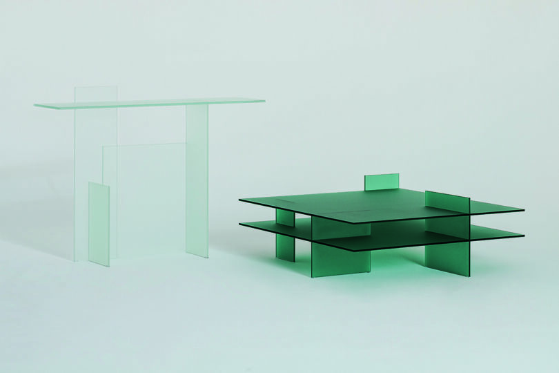 Two minimalist glass tables, one taller and clear, the other shorter and green, displayed against a plain background.