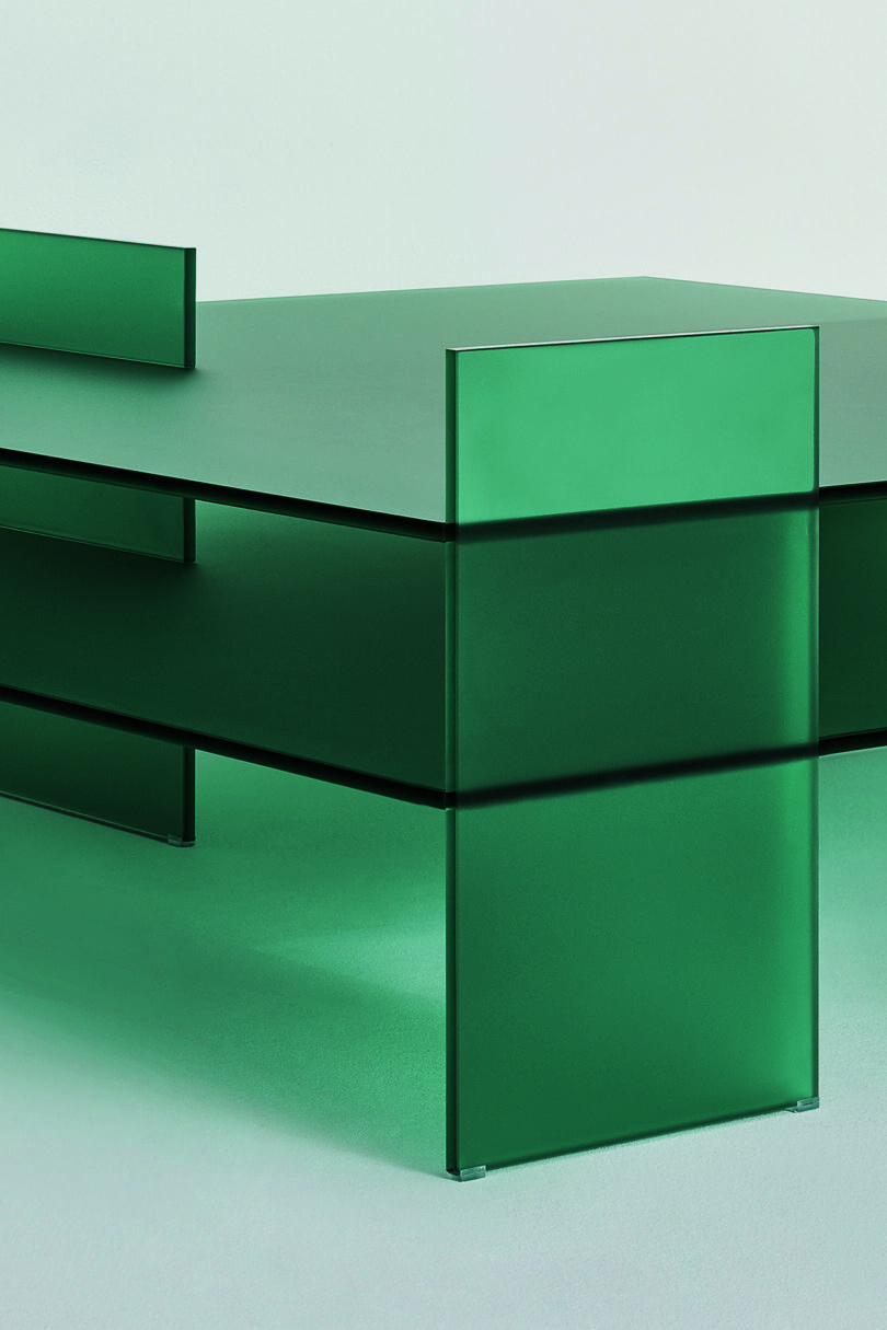 Detail of a minimalist green glass table displayed against a plain background.