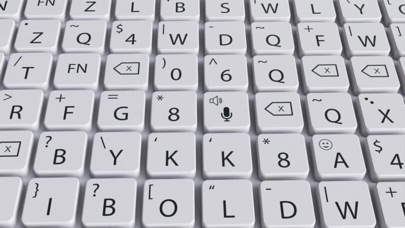A close-up view of a tactile keyboard with white keys displaying various symbols, letters, and icons, including a microphone icon in the center.