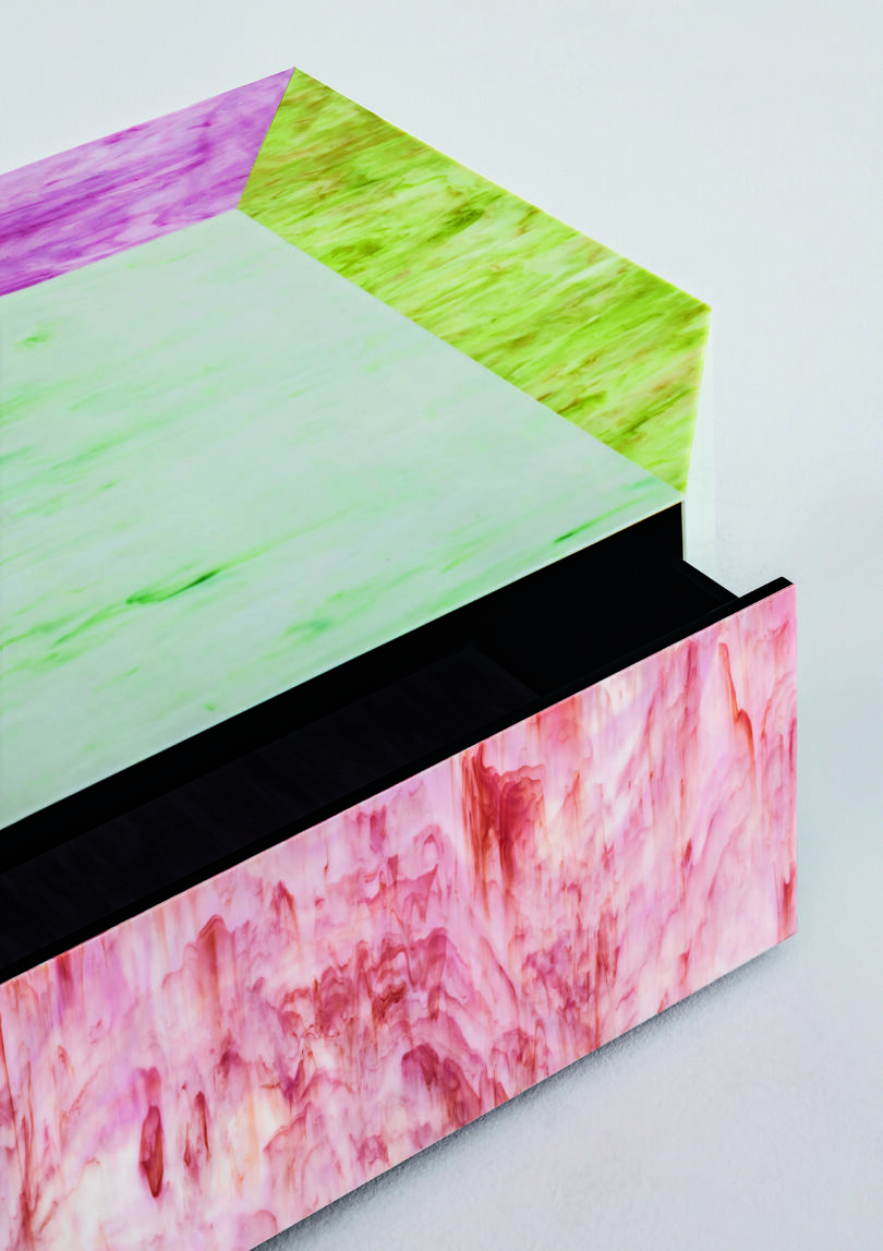 Detail of a multicolored geometric coffee table featuring shades of pink, green, and purple with a marbled texture on a plain background.