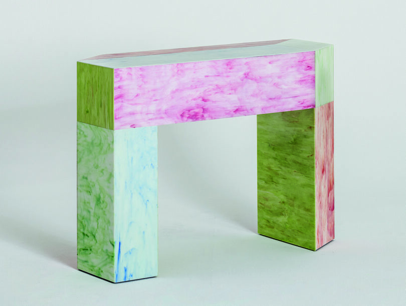 A multicolored geometric console featuring shades of pink, green, and purple with a marbled texture on a plain background.