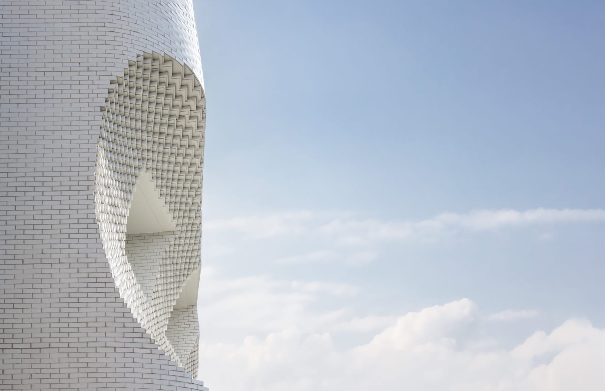 a detail of a concave form in a white brick facade, set against a blue sky
