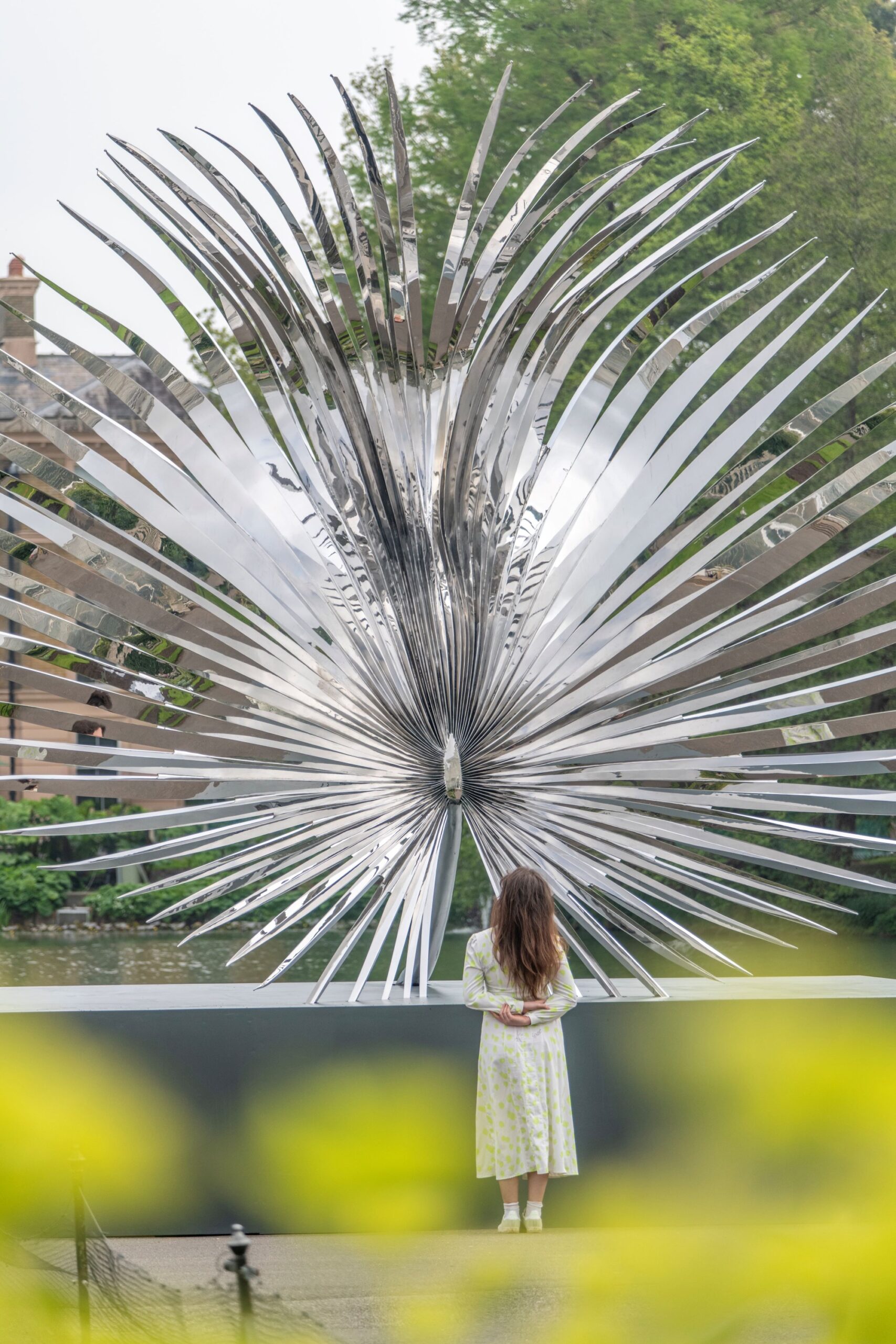 a woman stands with her back to us, viewing a larger-than-life outdoor sculpture of a tropical flower with numerous long, spiky petals
