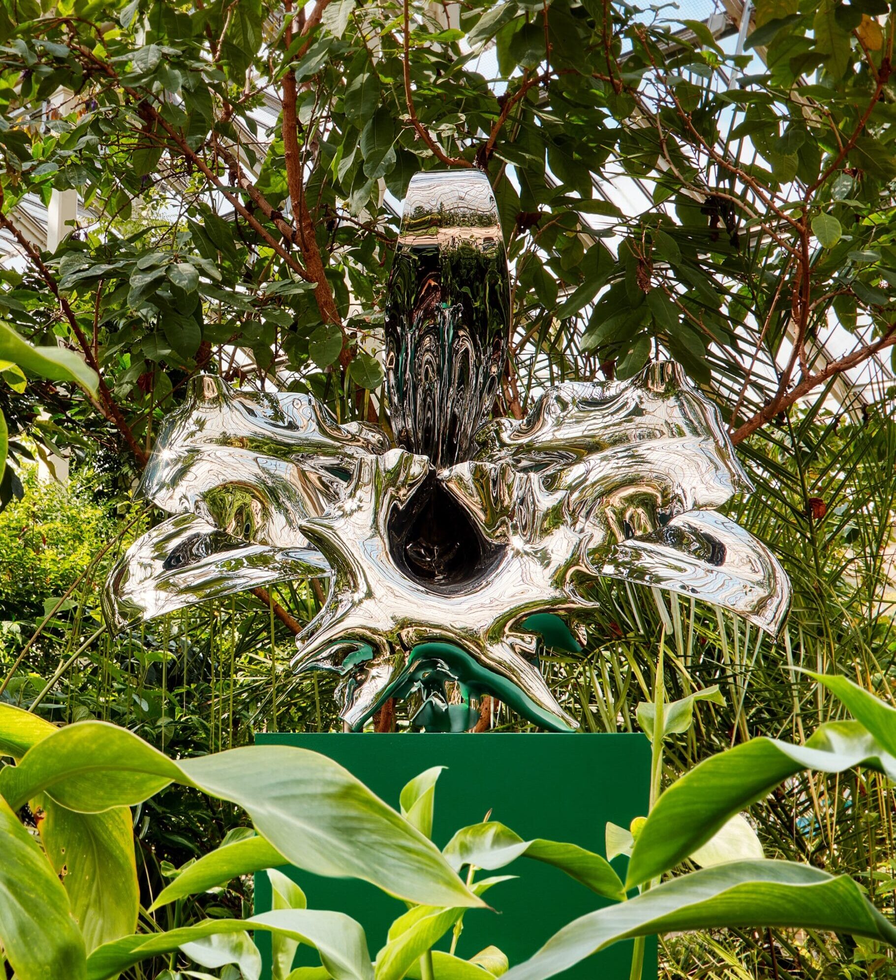 a larger-than-life sculpture of an orchid inside a greenhouse, surrounded by tropical plants