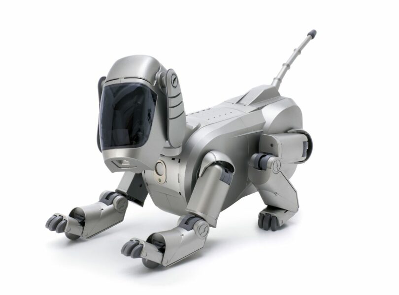 A silver robotic dog with a sleek design, featuring a large dark visor for a face and articulated limbs, posed on a white background