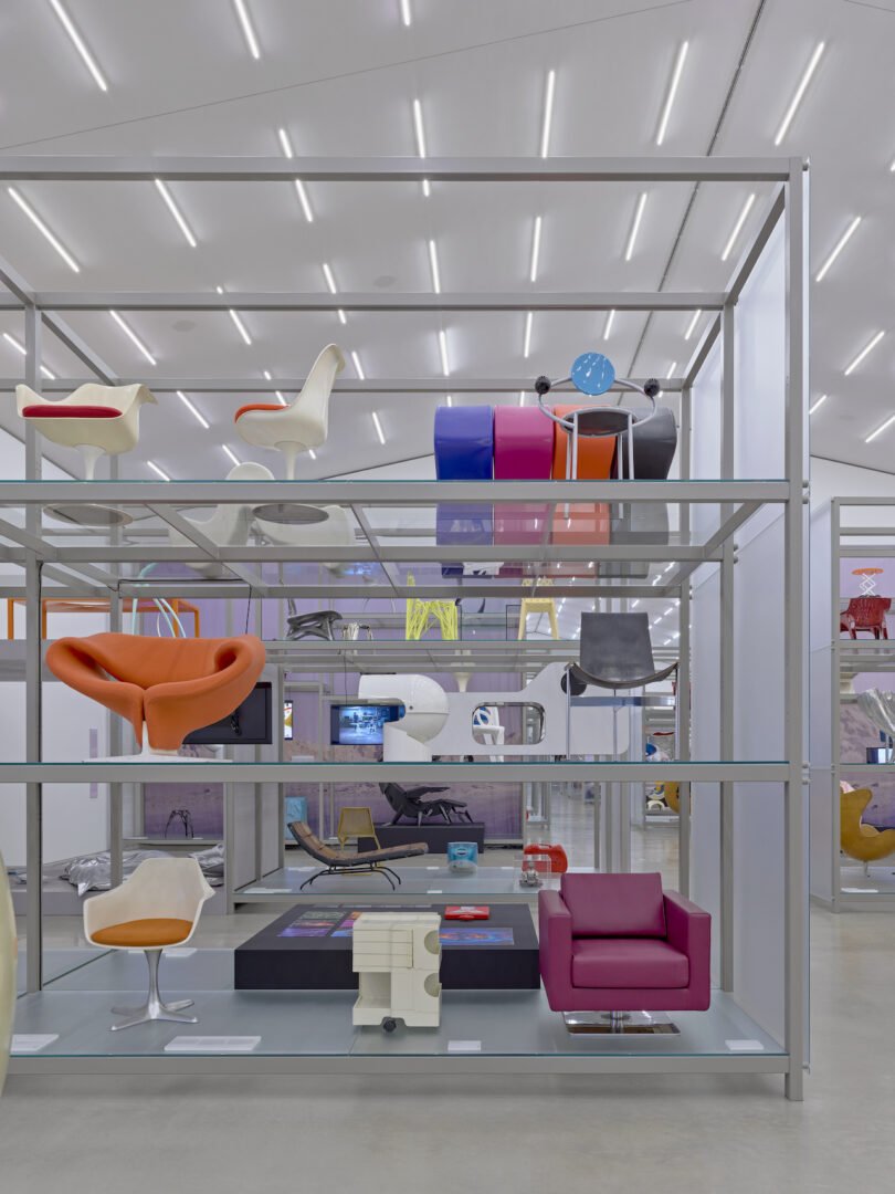 Shelves displaying various modern and colorful chairs in a well-lit exhibition space with a minimalist design