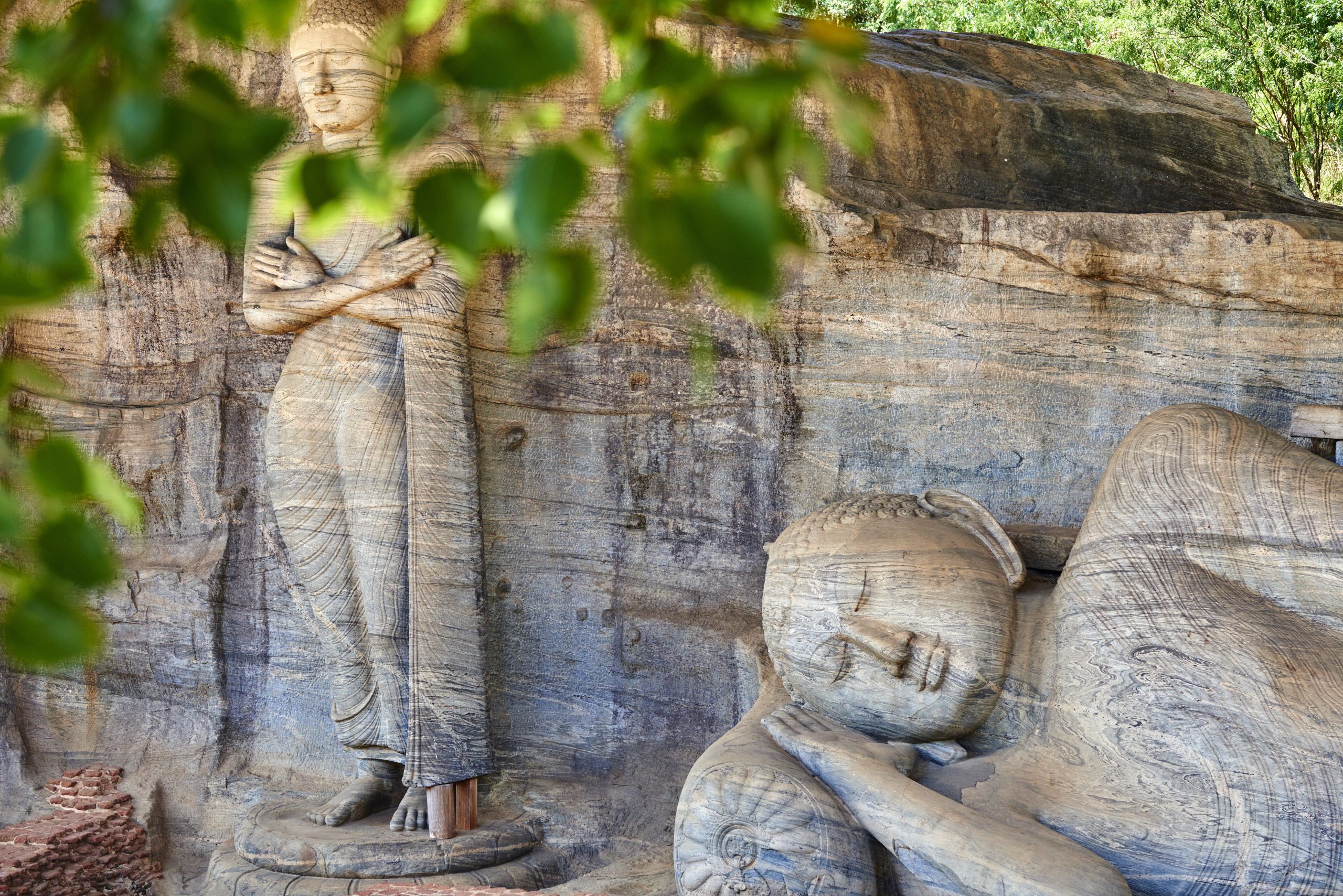 Monumental Buddha statues at the Gal Vihara temple complex, Polonnaruwa, Sri Lanka. Monumental Buddha statues viewed through the leaves at the Gal Vihara temple complex, Polonnaruwa, Sri Lanka.