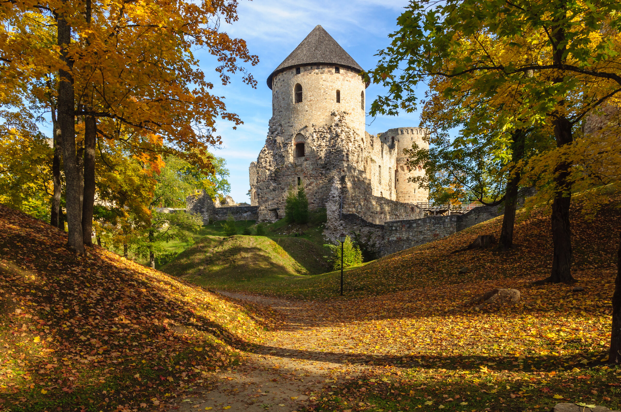 Latvia castle Medieval castle ruins sit in a forest where leaves are turning yellow in fall.