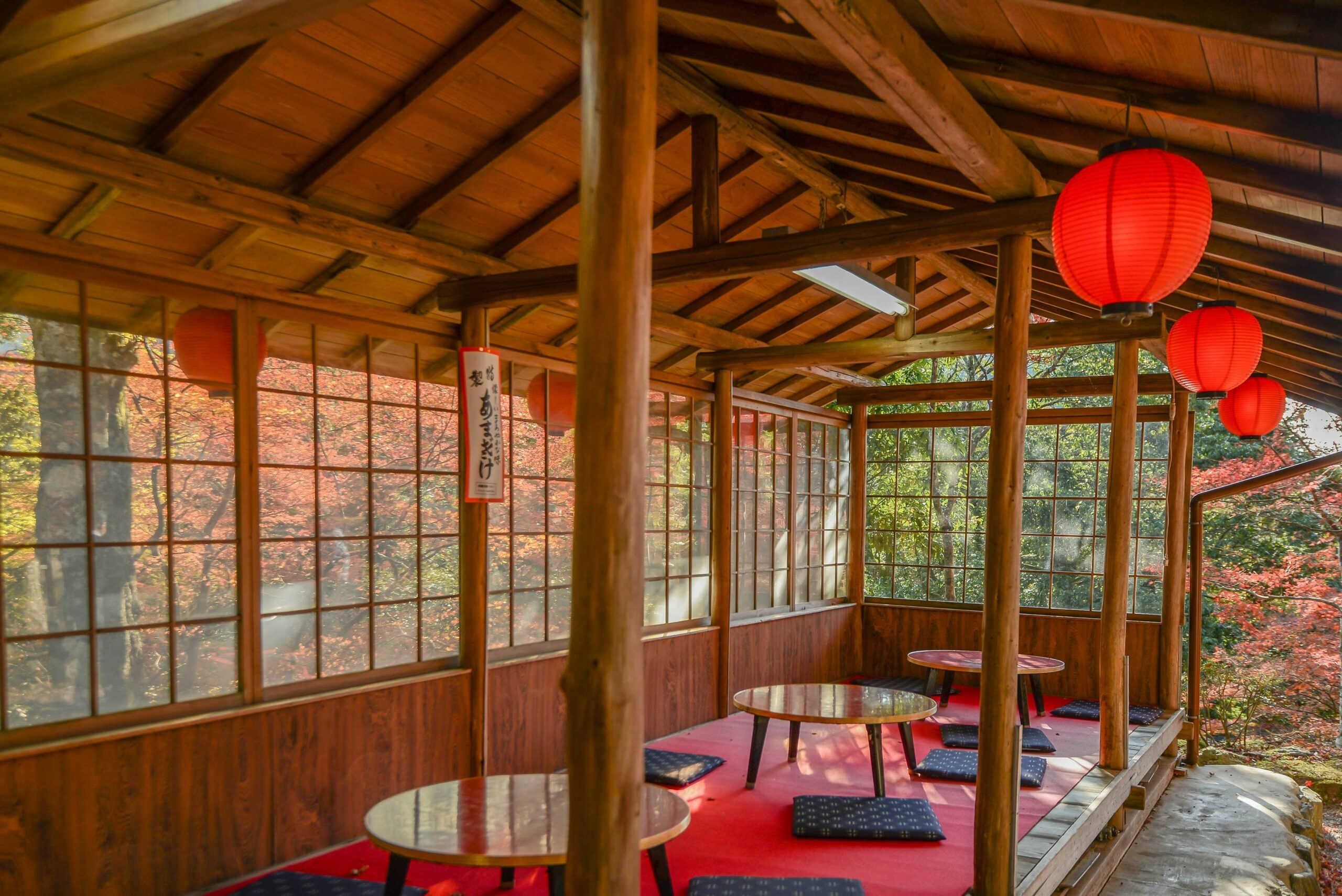 An open-sided structure with three low wooden tables and several cushions on the floor for kneeling on
